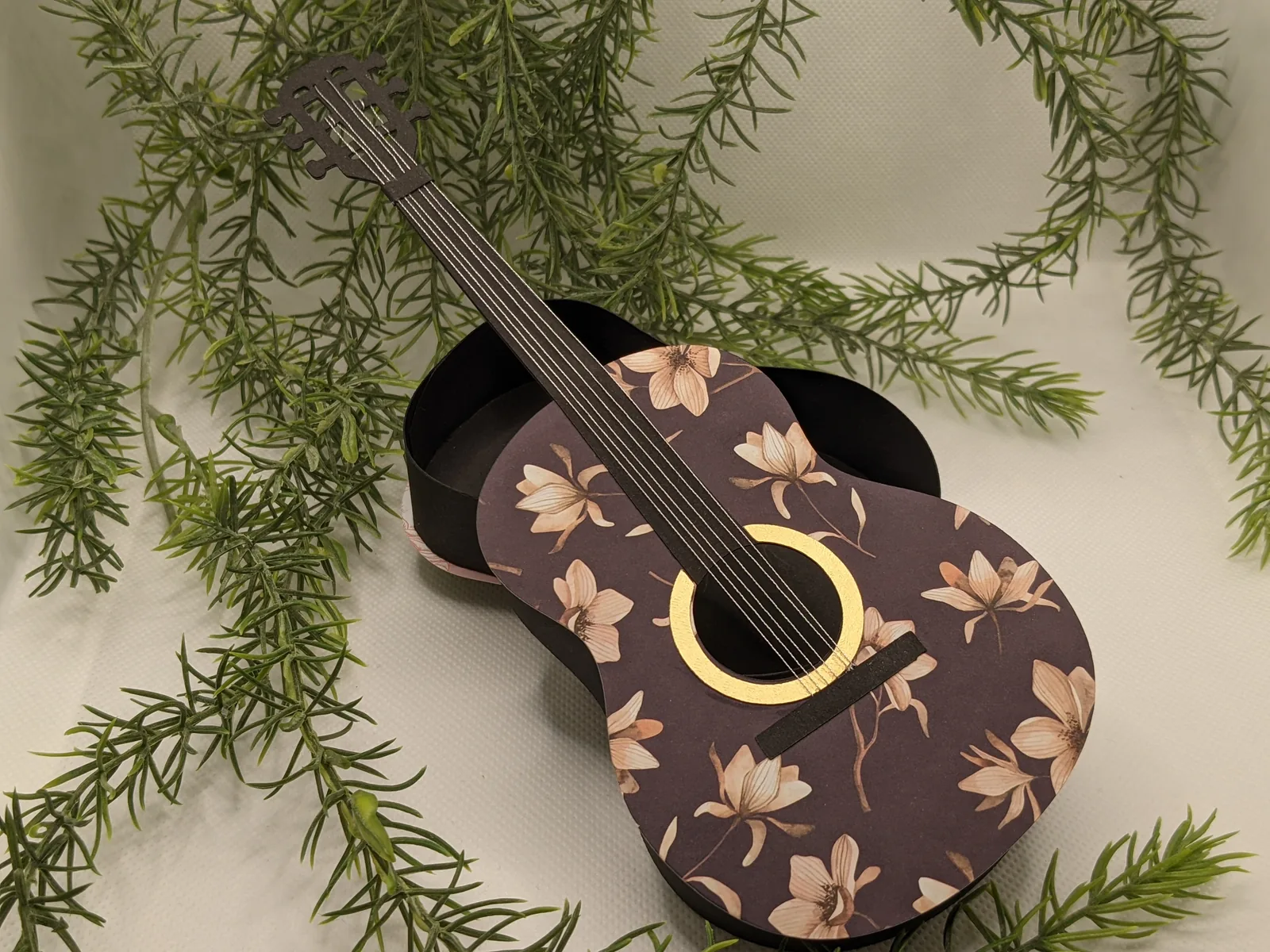 Geschenkverpackung in Form einer schwarzen Gitarre mit Blütenmotiv